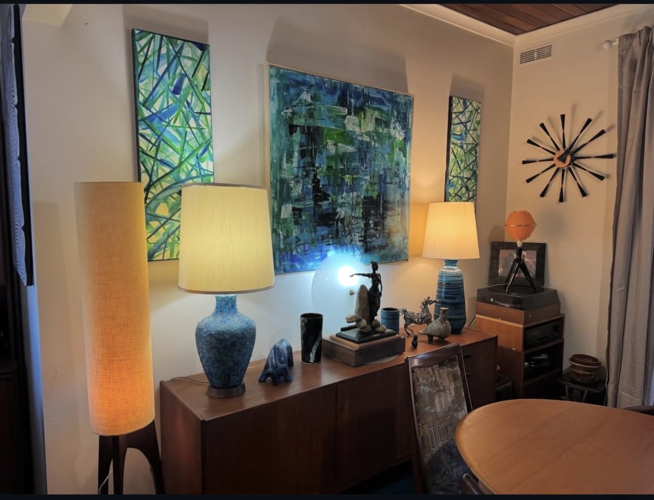 Pair of glowing blue ceramic table lamps on a teak sideboard with MVRArt23 original artworks in green and blue.
