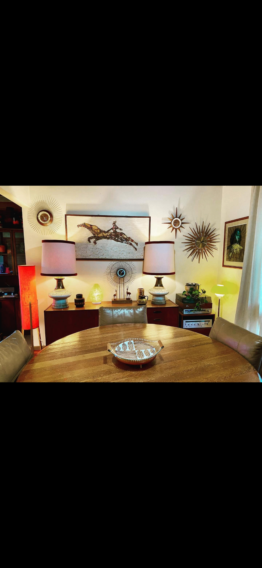 Pair of large restored Ellis Australia Fler 64 rocket lamps in front of a mosaic horse panel and a wall of sunburst clocks.